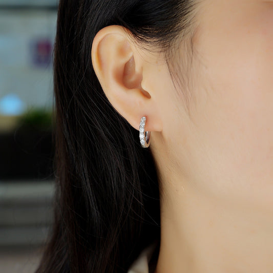 Close-up of an ear wearing a silver hoop earring with a blurred background
