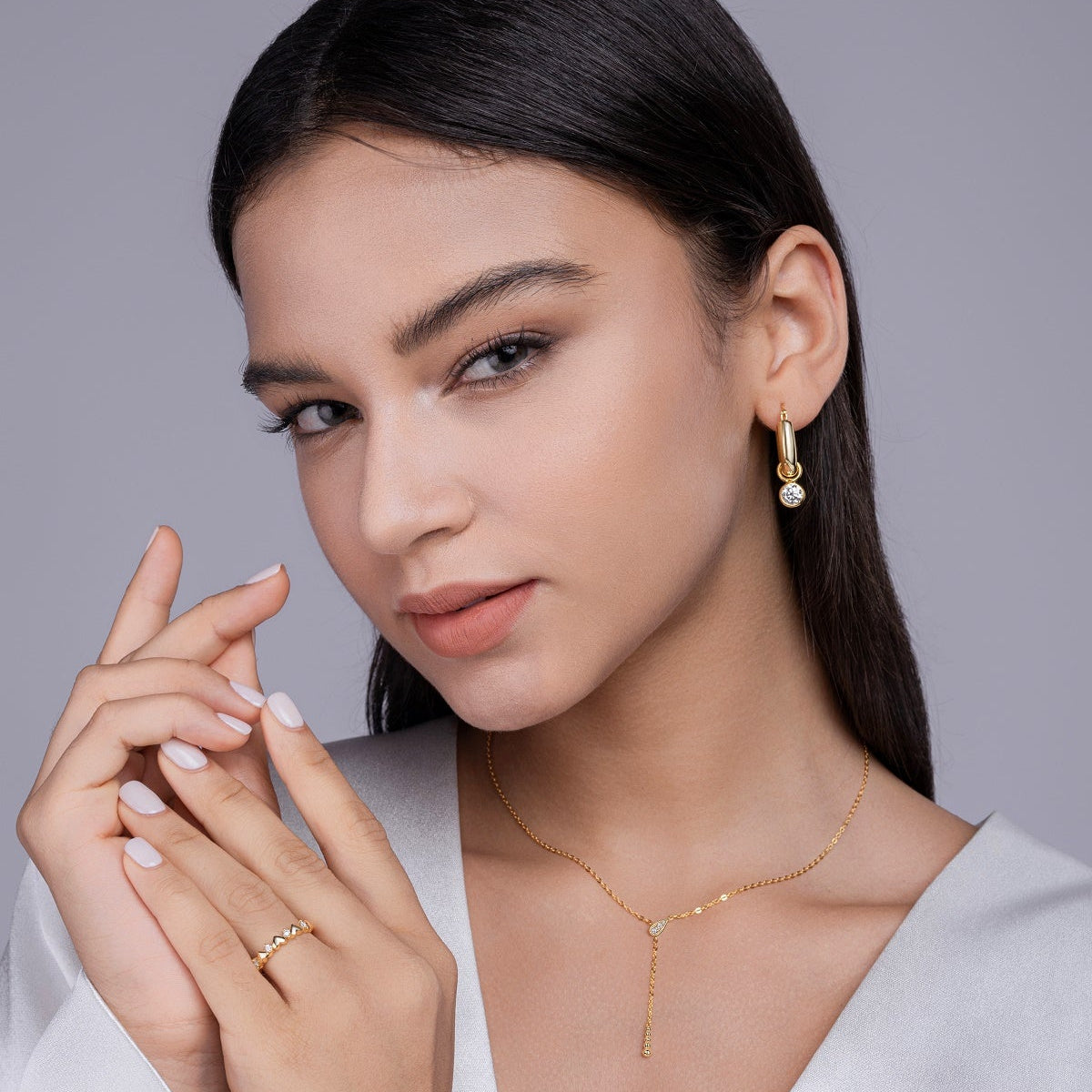Woman wearing gold jewelry including earrings and a necklace against a gray background