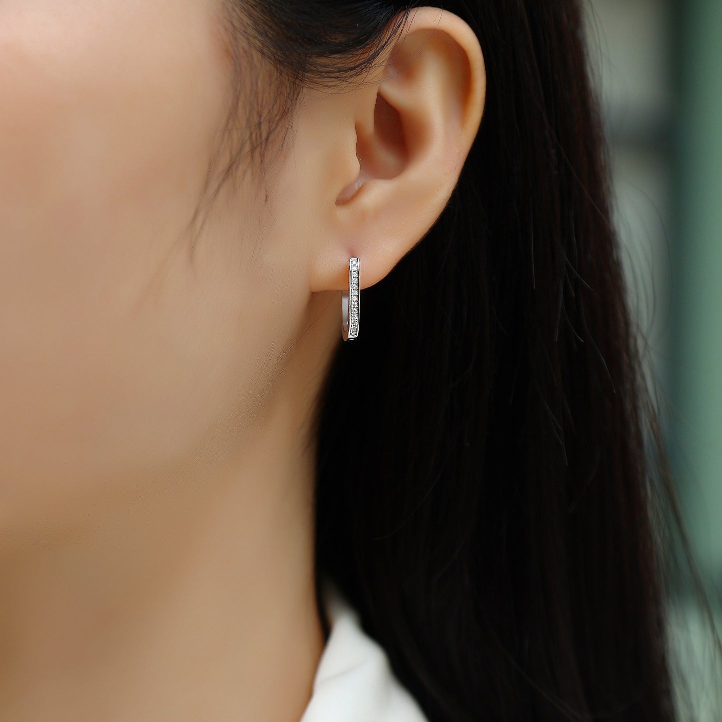 Close-up of an ear wearing a silver hoop earring with a blurred background