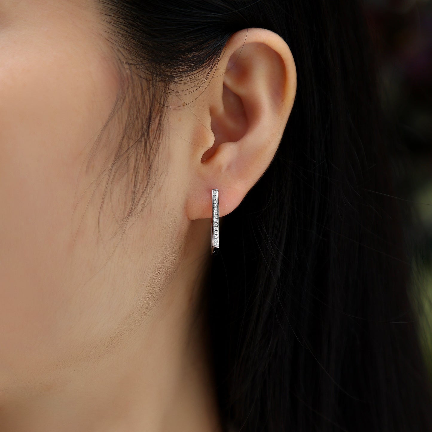 Close-up of an ear wearing a silver hoop earring with a blurred background