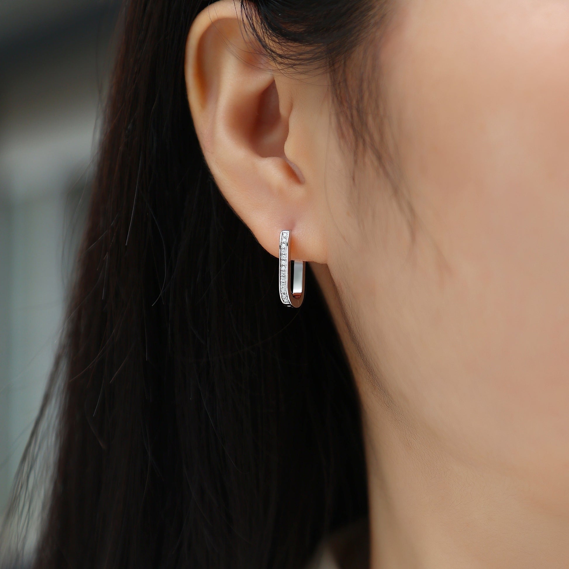 Close-up of an ear wearing a silver hoop earring with a blurred background