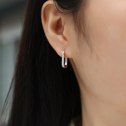 Close-up of an ear wearing a silver hoop earring with a blurred background